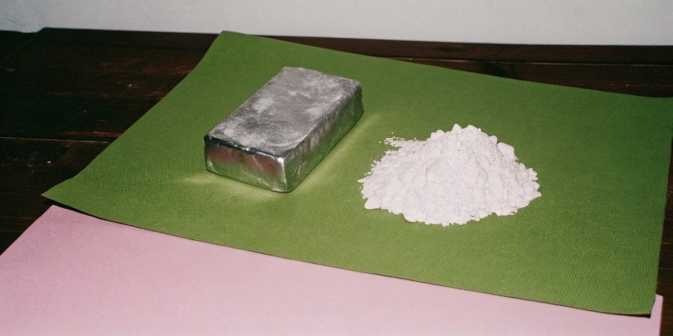 A shiny, solid aluminum ingot next to a sample of white aluminum hydroxide powder