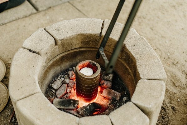 alt with keywords: A crucible containing aluminum being heated in a small, well-contained campfire