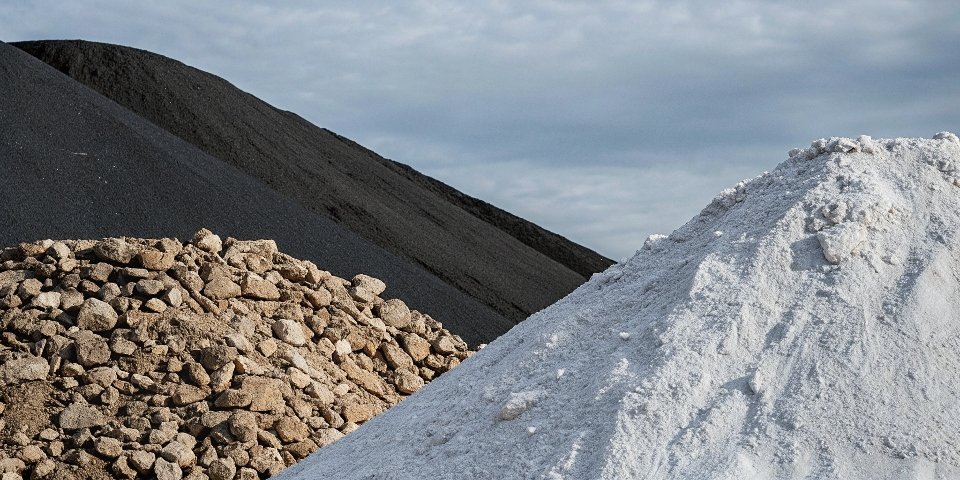 A pile of raw bauxite ore next to a pile of refined white alumina powder