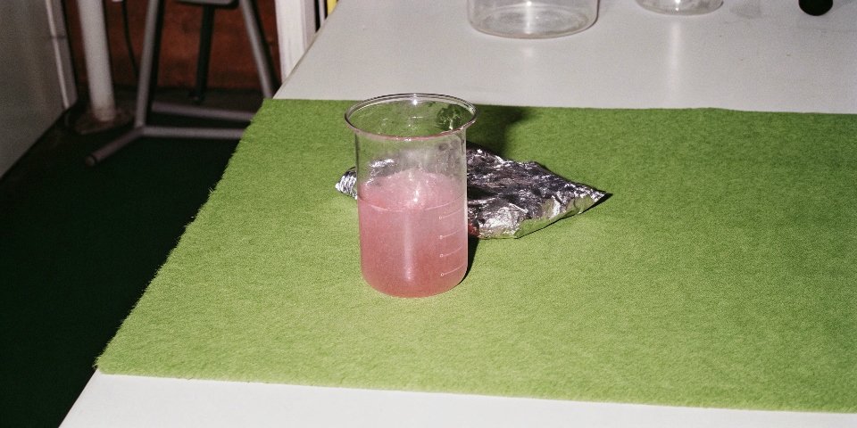 A piece of aluminum foil bubbling and smoking as it dissolves in a beaker of sodium hydroxide solution
