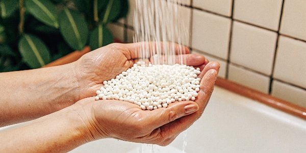 A handful of white activated alumina balls being rinsed under a stream of clean water