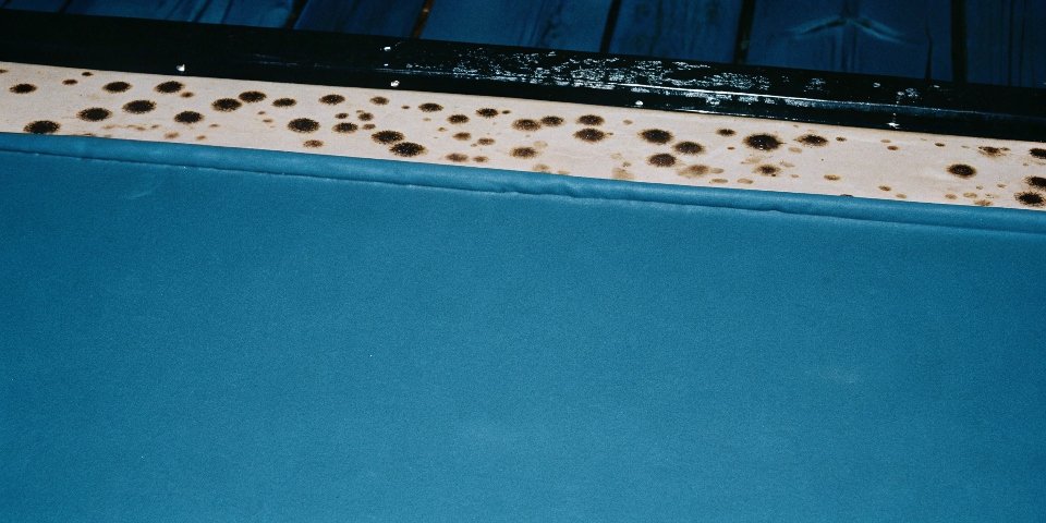A close-up view of an aluminum surface showing bubbles and corrosion where drops of NaOH solution have been applied