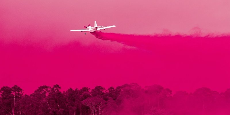 An aircraft dropping red fire retardant over a forest fire