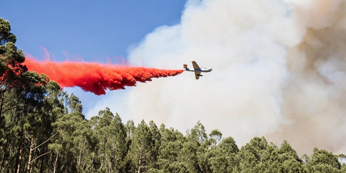 A photo of an airplane dropping the characteristic red slurry over a burning forest