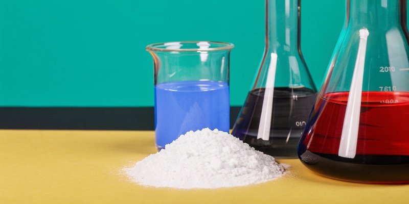 A photo of white aluminum hydroxide powder next to chemical beakers