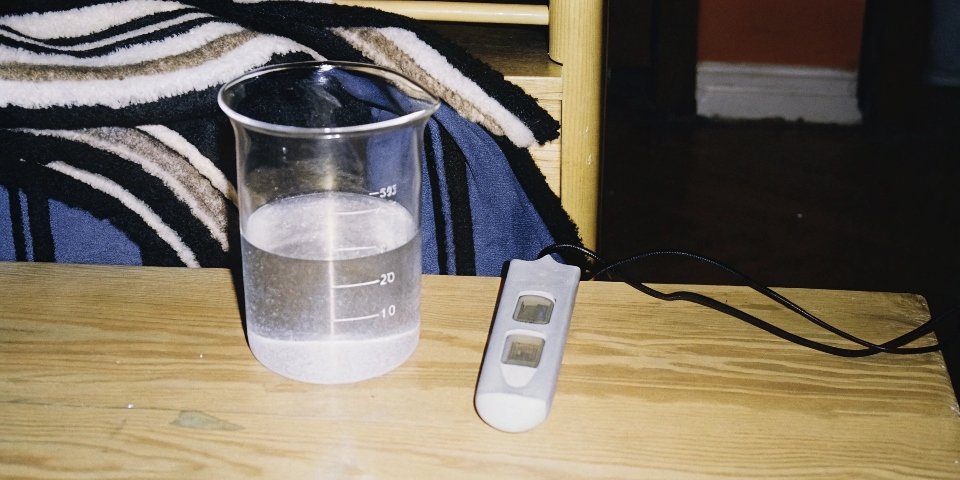 A lab beaker with a pH meter showing a neutral reading for water with aluminum hydroxide powder settled at the bottom