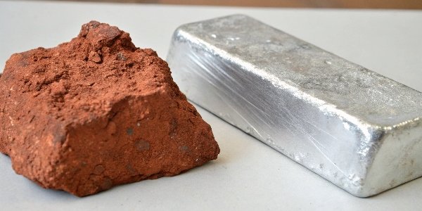 A piece of bauxite rock next to a pure aluminum ingot to show the transformation