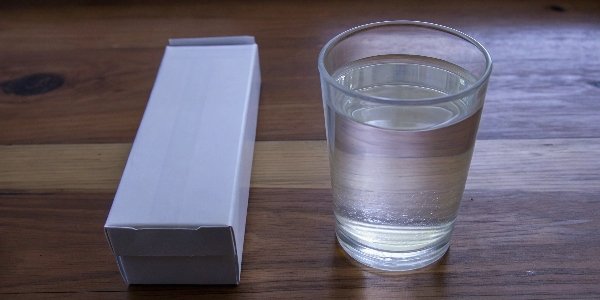 A product box of Almagel next to a glass of the liquid suspension