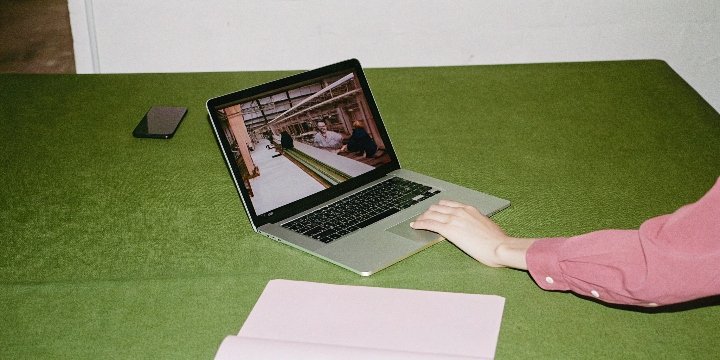 A person on a video call on a laptop, with a factory production line visible on the screen
