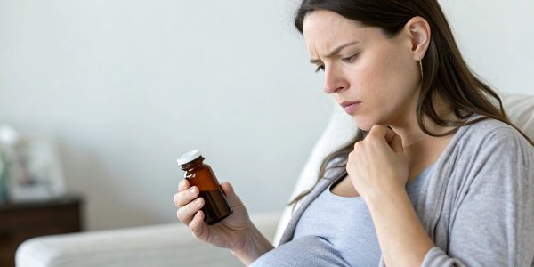 A pregnant woman looking at a medicine bottle with a question mark