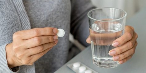 A person holding an antacid tablet with a glass of water.